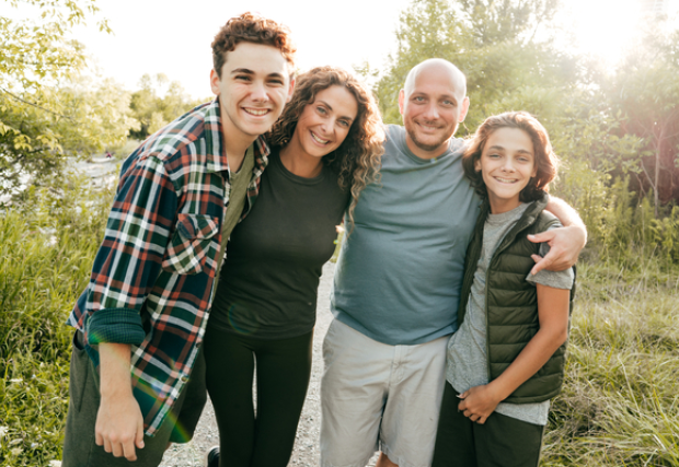 Father, mother and two sons smiling and standing in field