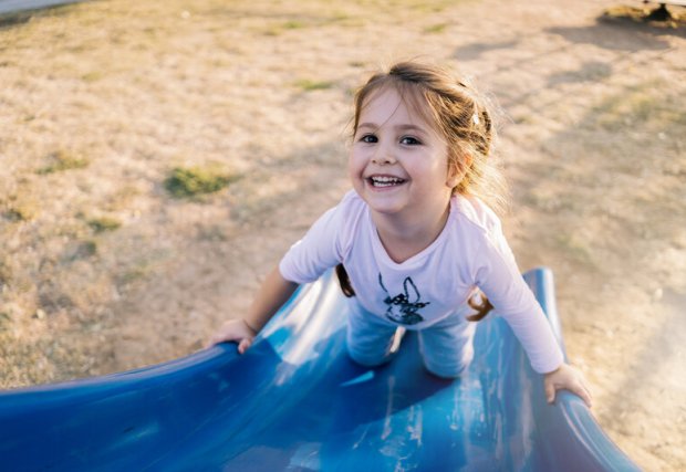 A young child on a slide, smiling up at the camera. 