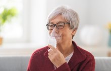 A woman doing a breathing treatment with a hand-held nebulizer