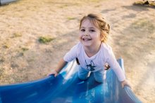 A young child on a slide, smiling up at the camera. 