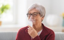 A woman doing a breathing treatment with a hand-held nebulizer