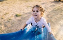 A young child on a slide, smiling up at the camera. 